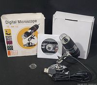 Digital microscope with LED light, adjustable metal stand, USB cable attached, software installation CD, and clear lens cover shown outside of original packaging - box included.