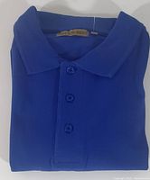 Frontal image of neatly folded royal blue cotton polo shirt showing buttons and collar.