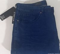 Close-up view of folded dark blue men's denim jeans with attached tags showing 'STRETCH' and brand label 'Tailored Recreation Premium'.