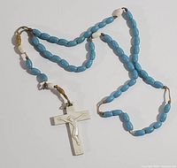 Full view of the light blue bead Catholic rosary laid out with white crucifix at the bottom.