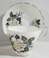Front view of Regency fine bone china teacup with floral design and matching saucer in background, showing delicate painted roses and gold edging.