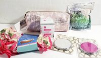 Photo showing all six new beauty accessory pieces including two compact mirrors, a cosmetics bag, exfoliating glove, facial scrub, and pack of cosmetic scrub pieces.