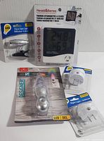 Lot of new plug-in night lights, clip-on spot light, and thermo-hygrometer with clock displayed together on white background.