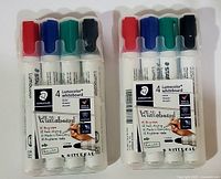 Two sets of STAEDTLER Lumocolor whiteboard markers, each including four markers in red, blue, green, and black, displayed in clear plastic holders, with visible branding on packaging.