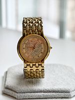 Front angled view of gold plated wristwatch showing case, bracelet, and crystal-set dial