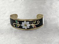 Front and full view of the silver cuff bracelet showing black background with mother of pearl flower and abalone shell inlay. Slight tarnishing on the metal visible.