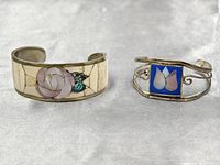 Two Alpaca silver cuff bracelets on light surface, showing decorative mother of pearl and enamel inlay designs