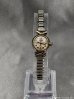 Full view of the Bulova ladies mechanical wristwatch on a display stand showing the metal expansion bracelet and round gold plated case.