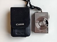 Canon IXUS II camera alongside black Canon PowerShot branded carrying case on white background.