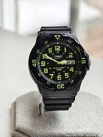 Front angled view showing black analog dial with luminous green large numbers, hands, and minute markers, with black resin strap and rotating bezel showing numbers and triangle in green.