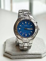 Front view of Fossil Blue men's watch with clear blue dial and stainless steel bracelet on stand.