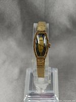 Full view of gold plated Gruen ladies watch on stand, showing overall shape and bracelet texture.