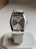 Front face view of Joan Rivers Classics watch showing silver dial, large Arabic numerals, and beige textured leather strap on display cushion.