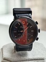 Black Kenneth Cole chronograph watch showing the entire watch including strap and metal case, placed on a stand.