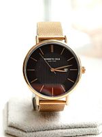 Front view of Kenneth Cole dress watch showing black dial with textured center, rose gold-tone markers, hands, and date window at 3 o'clock. Rose gold mesh band visible.