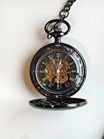 Front open view of black mechanical pocket watch showing transparent skeleton dial, Roman numerals, ornate hands, and partial view of internal gears with protective film on the face.