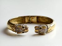 Photo of the gold tone dragon bangle showing the two dragon heads decorated with rhinestones and green stones for eyes.