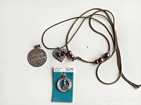 Three jewelry items on white background: necklace with heart-shaped pendant, round engraved pendant, small round crown pendant on blue backing