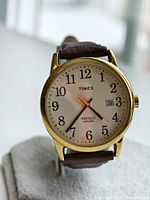 Front angle view of Timex Indiglo Easy Reader watch showing gold-tone case, white dial with black numerals, and brown leather strap