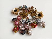 Top view of multiple vintage earclips with various designs including cream flower, bead clusters in pink, black, white, and turquoise, showing cosmetic wear.