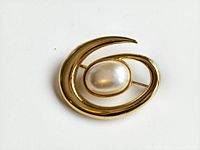 Close-up of vintage Monet pin brooch showing gold-tone swirl design with oval faux pearl center.