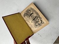 Open book showing a black and white illustration inside, with red cloth cover and yellow endpaper visible.