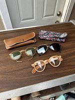Three pairs of vintage 1960s men’s glasses frames on a table with their cases, showing different frame styles and materials.
