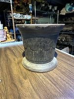 Side view of antique cast iron mortar showing flared lip and decorative embossed band with vertical ridges.