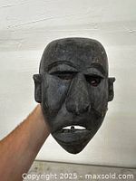 Front view of dark wooden mask showing facial features: prominent nose, open mouth, carved eyebrows and ears.