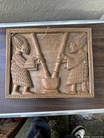 Front view of the rectangular wooden panel showing two carved African figures working with pestles on a mortar.