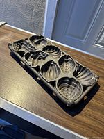 Top view of cast iron seashell mold on wooden surface under sunlight.