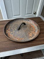 Front and top angle view of a cast iron Dutch oven lid, showing rust patches and handle.