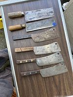 Top view of six antique cleavers showing mixed wooden and rosewood handles, blades display age wear and patina.
