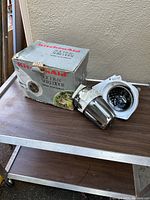 Photo showing the KitchenAid Slicer & Shredder attachment next to the original box on a wooden surface.