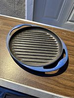 Oval blue enamel coated cast iron broiler pan griddle with ridged cooking surface and handles.