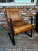 Full view of brown leather accent chair with visible ribbed stitching and black metal sled base frame, showing overall design and condition.