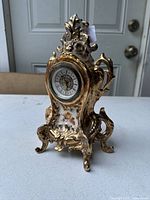 Front and angled view of the ornate porcelain clock showing gold accents and floral designs.
