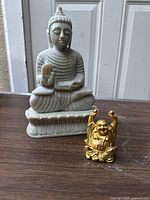 Both Buddha statues photographed together on a wooden surface against a neutral background, showing size difference and details.