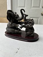 Front angled view showing both elephant statues sitting on wooden base interacting with raised trunks