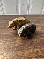 Two diecast souvenir bears on a wooden surface, one gold-colored with a scenic plaque, the other silver/bronze-colored with a Crater Lake plaque.