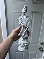 Full view of the porcelain Guanyin statue held by hand in front of a door, showing the whole figure and base.