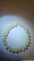 Photo of white jade bracelet with round 6mm beads on elastic band, shown on a neutral background with spotlight highlighting bead translucency and quality.