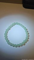 Top view of the natural green aventurine bracelet arranged in a circular shape on a light surface with spotlight effect showing bead color and texture.