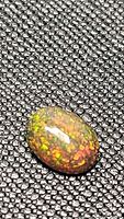 Oval cabochon on textured surface showing red and green pinfire play-of-color