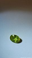 Oval cut natural African sphene gemstone with bright green-yellow color and visible brilliance on a plain background under direct light.