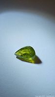 Top view of pear cut apple green peridot gemstone on white surface with shadow.