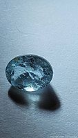 Natural untreated sky blue aquamarine gemstone viewed under direct light showing internal inclusions and oval cut shape.