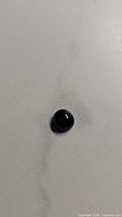 Photo of the polished round black gemstone showing its domed cabochon shape on a white background.