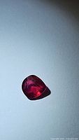 Top-down view of loose pear-shaped red gemstone showing facets and internal inclusions
