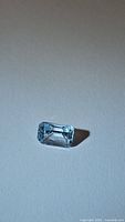 Close-up photo of the natural blue topaz gemstone showing emerald cut shape, clarity and sky blue color on white background.